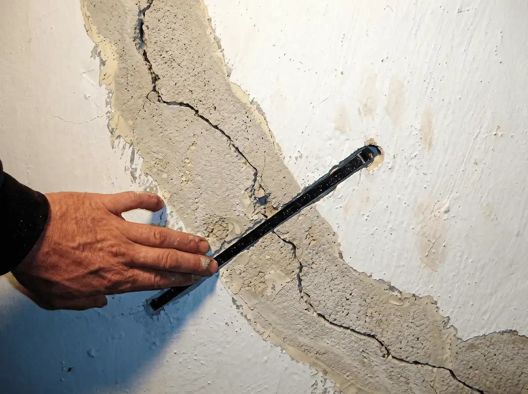 A wall with a large crack is being inspected by a professional in Kansas City, MO